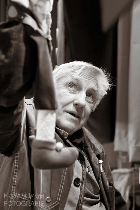 Ein alter Mann mit einer Kasperpuppe in der Hand hinter seinem Puppentheater.
