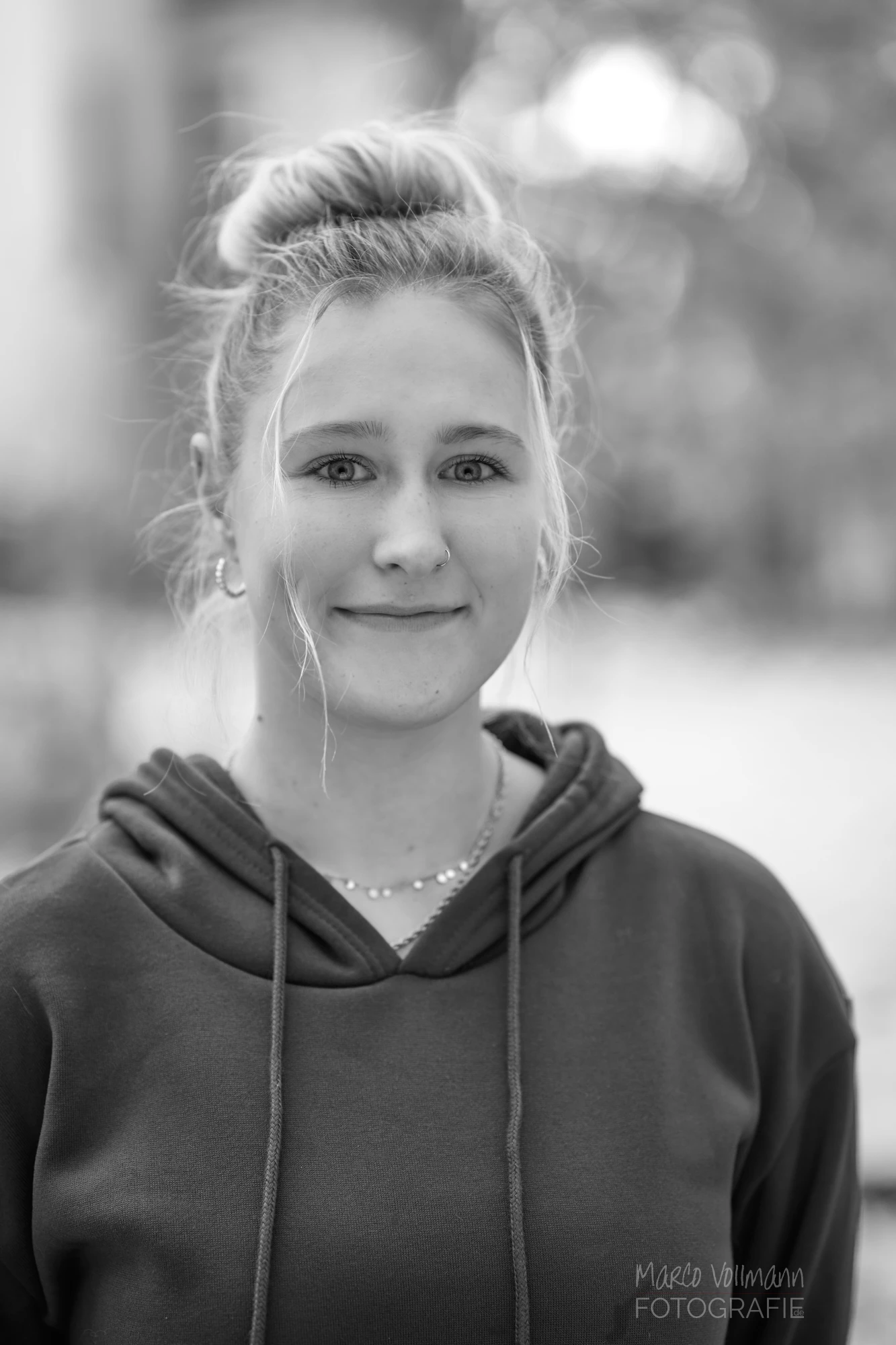 Ein schwarz-weißes Foto einer jungen blonden Frau in dunklem Kaputzenpulli.