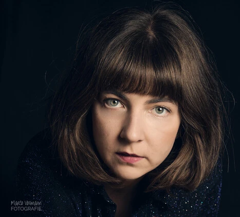 Eine junge Frau mit Bobfrisur vor schwarzem Hintergrund schaut in die Kamera.